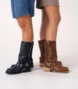 Bota de caña media confeccionada en cuero vacuno color marrón oscuro, con diseño de estilo biker. Presenta una tira decorativa con hebilla metálica y estribo desmontable en la zona del tobillo, taco cuadrado de madera y suela de caucho.