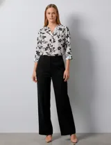 Blusa de gasa con estampado floral en tonos blanco y negro, cuello a la base con escote en V y cierre frontal parcial con botones. Presenta mangas tres cuartos con puños rectos.