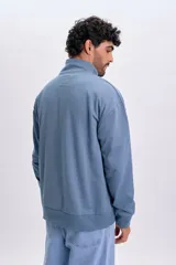 Buzo deportivo color azul piedra, con cuello alto, cierre frontal parcial y mangas largas con puños elásticos.