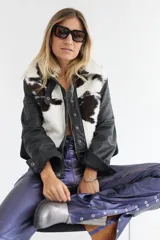 Chaqueta de cuero negro con paneles frontales y cuello de piel de vaca (estampado marrón y blanco). Presenta cierre frontal de cremallera y botones a presión.