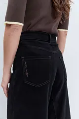 Jeans de tiro alto en color negro, con diseño de corte acampanado y paneles godet que aportan amplitud en el bajo. Presenta costuras visibles y cierre frontal con botón y cremallera.