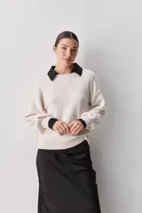 Sweater negro de tejido suave con escote redondo, mangas largas y calce relajado, con terminaciones acanaladas en cuello, puños y ruedo.