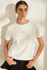 Remera marrón de manga corta y cuello redondo, con detalles de costuras decorativas en contraste color crudo en el cuello, los puños y el dobladillo inferior. Cuenta con el nombre de la marca impreso en el pecho.