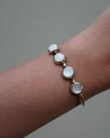 Pulsera rígida dorada con cuatro piedras redondas de nácar engarzadas.