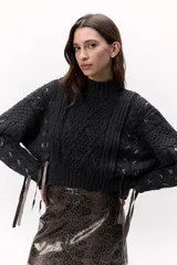 Sweater de lana merino tejido en punto grueso, color gris oscuro, con cuello alto. Presenta un diseño calado con tientos de cuero marrón insertados a lo largo de la prenda, simulando un lazo o detalle orgánico.