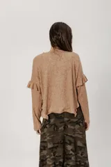 Buzo color beige de punto con lanilla tipo canelón, corte holgado y mangas largas con volados en los hombros.