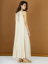 Vestido largo color crema de lurex plisado, con cuello halter y corte recto.