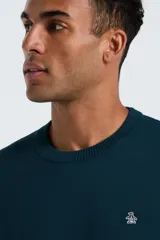 Sweater de punto color verde oscuro, con cuello redondo, mangas largas y puños acanalados. Presenta un pequeño logo bordado en el pecho.