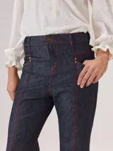 Jean de corte recto confeccionado en denim azul oscuro, con costuras a la vista en color rojo contrastante. Presenta un diseño de tiro alto con bolsillos frontales y cierre de botón.