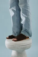 Sandalia mule de gamuza marrón, de una sola pieza con diseño asimétrico, punta cuadrada y suela plana.