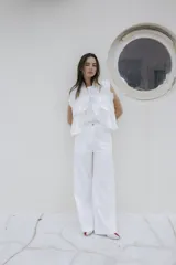 Pantalón de lino blanco de pierna amplia y corte recto, con bolsillos frontales y cierre de botón.