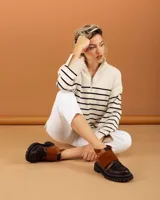 Botinetas de caña baja con suela track gruesa, combinando cuero negro en la puntera, gamuza marrón en el lateral y detalles de textura animal print tipo serpiente en tonos marrones. Presenta un cierre de solapa con velcro en el empeine.