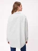 Camisa de corte oversize con diseño a rayas verticales en tonos azul y blanco. Presenta cuello clásico, cierre frontal con botones y un bolsillo en el pecho con detalle de etiqueta.