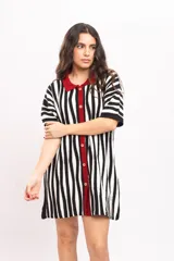 Vestido camisola corto de tejido fresco de algodón, con diseño de rayas verticales en blanco y negro. Presenta cuello polo, solapa y ribete central con botones en color rojo.