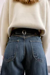 Jeans de tiro medio, color azul oscuro lavado, con corte balloon fit (holgado en muslos y estrechado en el tobillo). Presenta cinco bolsillos, cierre frontal con botones y detalle de trabilla con hebilla en la parte trasera de la cintura.