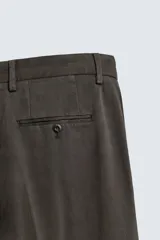 Pantalón relaxed fit de traje color marrón oscuro, confeccionado en tejido con mezcla de algodón. Cuenta con bolsillos frontales, bolsillos traseros de doble vivo con botón y efecto lavado. Cierre frontal con cremallera y botón.