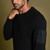 Sweater de punto negro con cuello redondo y manga larga. Presenta un bolsillo con cierre en la manga izquierda.