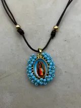 Collar ajustable con cordón azul y dije central ovalado con imagen religiosa, rodeado por una estructura de cuentas multicolores.