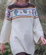 Vestido midi de punto color marfil, confeccionado artesanalmente en lana merino, con silueta en A, mangas largas oxford y cuello a la base. Presenta un diseño de bloques de color con bordados hechos a mano con motivos paisley y florales en tonos marrones, azules y rosados en la parte superior y las mangas.
