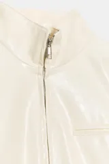 Chaqueta corta de efecto piel en color crema, con cuello subido, manga larga y cierre frontal con cremallera. Presenta bolsillos de vivo en el pecho y en la parte delantera.