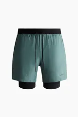 Short deportivo de doble capa color verde con calzas cortas negras incorporadas en el interior. Cuenta con tecnología DryMove™, cintura elástica negra con cordón ajustable, bolsillos laterales y aberturas en el bajo.