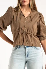 Blusa blanca de algodón con delicado bordado floral, mangas abullonadas de largo 3/4 y cierre frontal con botones y cordón ajustable en la cintura.