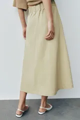 Falda midi de tiro alto color beige, con bolsillos delanteros, cintura con trabillas y cierre frontal con cremallera y ganchos metálicos.