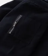 Campera de sarga de algodón con capucha, cierre frontal con cremallera y trabas metálicas decorativas. Presenta un bolsillo con cierre en la manga y puños elásticos, con un diseño de estilo utilitario.