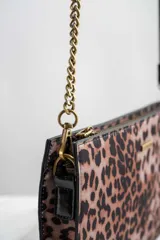 Cartera tipo sobre con estampado animal print, correa de cuero sintético negra y cadena dorada.