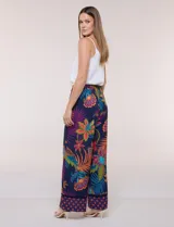 Pantalón pull on largo de caída fluida, cintura alta con pretina trasera elastizada, pierna de corte ancho tipo palazzo y detalle de guarda geométrica sobre el ruedo inferior, con estampado floral multicolor sobre base azul.