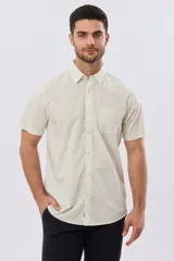 Camisa lisa de algodón azul marino, de manga corta, con cuello camisero, cierre frontal de botones y un bolsillo aplicado en el pecho.