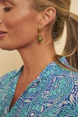 Aros colgantes dorados con diseño superior de trébol texturizado y cuenta esférica verde esmaltada con detalles decorativos.