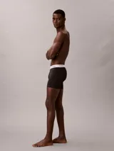 Pack de tres bóxers Calvin Klein tipo boxer brief de algodón elástico. Incluye un modelo negro con monograma estampado, uno azul oscuro liso y uno gris claro liso. Todos cuentan con cintura elástica blanca con el logo de la marca.
