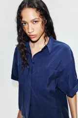 Camisa de cuello solapa y manga corta con dobladillo, presenta bolsillos de plastrón en el frente, bajo asimétrico y cierre frontal con botones ocultos.