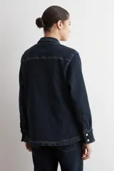 Camisa de jean de corte recto y calce holgado, con cuello clásico, cierre frontal con botones metálicos y dos bolsillos delanteros con solapa y botón.
