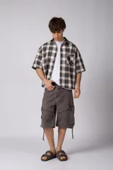 Camisa de manga corta de popelina cuadrillé en tonos marrón, blanco y gris, con diseño boxy fit, cuello camisero, cierre frontal de botones, bolsillo en el pecho con detalle bordado y dobladillo recto.