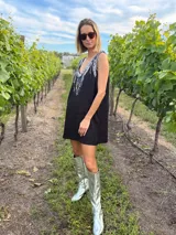 Vestido corto negro de gabardina con corte suelto y escote en V en frente y espalda. La parte delantera está adornada con flecos de lentejuelas plateadas.