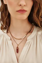 Collar doble de metal dorado compuesto por una cadena tipo serpiente y una cadena fina con dije de piedra sintética roja en forma de punta envuelta en alambre.