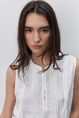 Blusa sin mangas color negro, de silueta fluida, con cuello redondo, detalle de alforzas en el frente y abotonadura parcial con botones visibles.