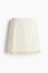 Pollera mini de tejido bouclé color crema, de tiro alto con elástico oculto en la cintura y bajo desflecado.