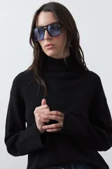 Polera de tejido liviano en color negro, con cuello alto, mangas largas y corte relajado. Presenta un diseño minimalista con recortes laterales que aportan estructura a la prenda.