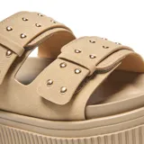 Sandalias plataforma tipo mule color taupe, con dos tiras anchas adornadas con hebillas cuadradas y remaches plateados decorativos. Cuenta con suela de plataforma alta con textura acanalada.