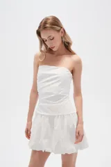 Vestido corto strapless de color blanco, con diseño drapeado en el torso y falda estilo globo con ruedo voluminoso.