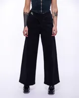 Pantalón de denim negro con corte sastrero de pierna ancha y tiro alto. Presenta una pretina cruzada con un aplique metálico de bronce en forma de caballo y cierre frontal invisible.