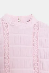 Camisa rosa de cuello alto, mangas cortas abullonadas y detalles de encaje y entredós en el frente y las mangas.