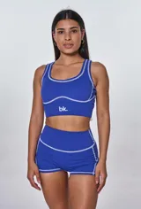 Conjunto deportivo compuesto por un top de escote redondo y un short de tiro alto, ambos en color azul con costuras decorativas a la vista en color blanco. El top presenta el logo de la marca estampado en el frente.