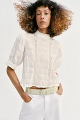 Camisa rosa de cuello alto, mangas cortas abullonadas y detalles de encaje y entredós en el frente y las mangas.