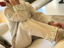 Pijama de viyela de algodón color beige con rayas verticales finas. El conjunto incluye una camisa de manga larga abotonada con detalles de estampado floral en puños y bolsillo, y un pantalón a juego con el mismo estampado floral en los bajos.