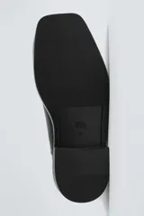 Bota tipo Chelsea de cuero negro con paneles elásticos laterales, suela de goma con volumen y detalle de pieza metálica en la puntera.