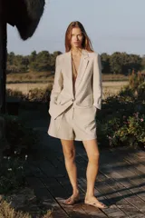 Blazer blanco de lino con cuello solapa, manga larga con hombreras y puños con vuelta estampada. Tiene bolsillos delanteros con solapa y cierre frontal con botón.